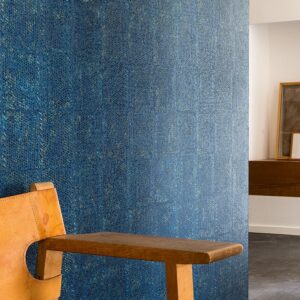 Blauw Elitis-behang Laca Salvaje met textuurpatroon in een modern interieur met houten stoel.