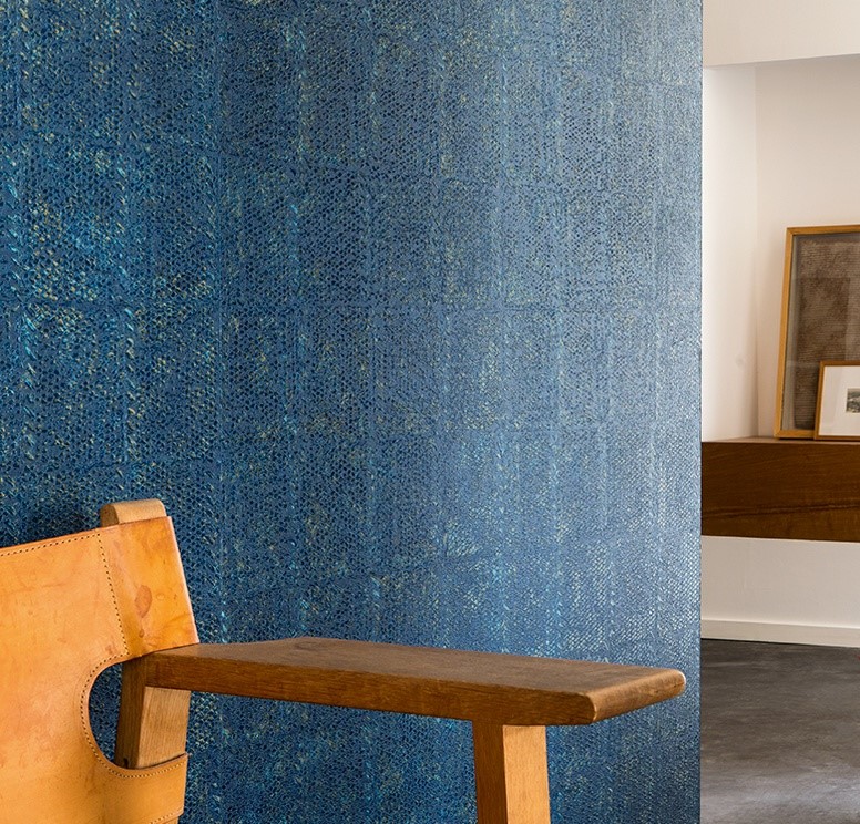 Blauw Elitis-behang Laca Salvaje met textuurpatroon in een modern interieur met houten stoel.