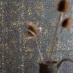 Detail van Elitis-behang Laca Salvaje in zwart met goudaccenten en vaas met gedroogde bloemen op de voorgrond.