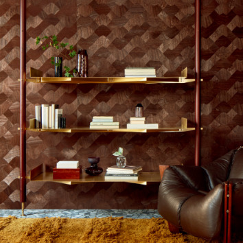 Interieur met Elitis-behang uit de Marqueteries-collectie in een warme bruine tint met grafisch patroon, gecombineerd met een leren fauteuil en een moderne wandplank.