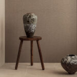 Keramische vaas op houten kruk tegen Elitis Lin Plâtre Innocent behang in een minimalistisch interieur.