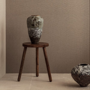 Keramische vaas op houten kruk tegen Elitis Lin Plâtre Innocent behang in een minimalistisch interieur.