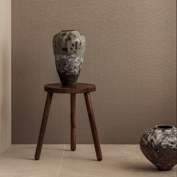Keramische vaas op houten kruk tegen Elitis Lin Plâtre Innocent behang in een minimalistisch interieur.