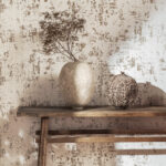 Beige Elitis Lin Plâtre behang met artistieke textuur, gecombineerd met rustieke vaasdecoratie op een houten plank.