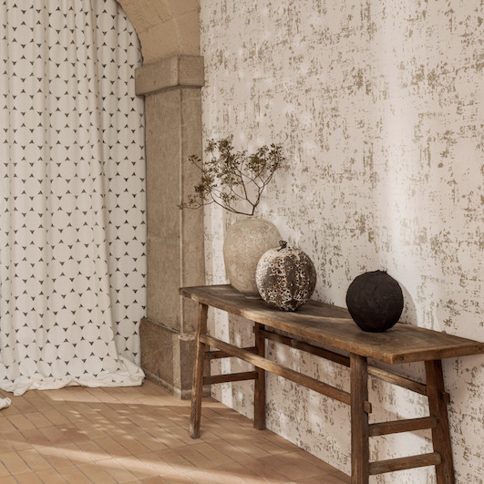 Rustieke sfeerhoek met Elitis-behang Lin Plâtre Toile d'artiste, houten bank en decoratieve vazen.