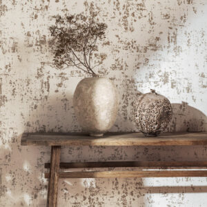 Beige Elitis Lin Plâtre behang met artistieke textuur, gecombineerd met rustieke vaasdecoratie op een houten plank.