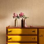 Kast met gele lades voor Elitis Madagascar-behang, versierd met bloemen in metallic vazen.