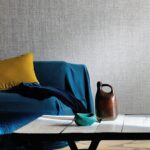Zithoek met blauw gedrapeerde bank, okergeel kussen en Elitis behang Madagascar op de achtergrond.