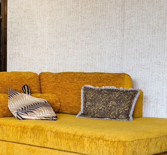 Gele fluwelen bank met sierkussens tegen een muur met Elitis-behang in de stijl Natural Mood.