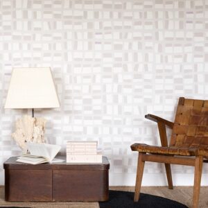 Interieur met Elitis-behang New Age, een houten stoel, vintage kist, tafellamp en boeken.