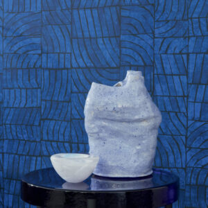 Blauw Elitis-behang uit de Voile de Papier-collectie met abstract patroon, gecombineerd met een keramische vaas en kom op een glanzende tafel.