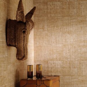 Interieur met Elitis-behang Raffia, een decoratief rieten paardenhoofd aan de muur en twee glazen op een leren kist.