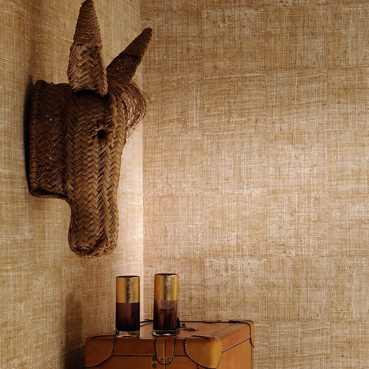 Interieur met Elitis-behang Raffia, een decoratief rieten paardenhoofd aan de muur en twee glazen op een leren kist.