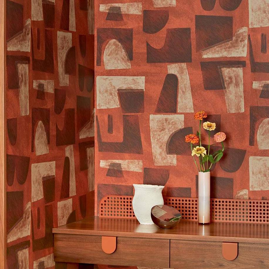 Decoratieve hoek met Elitis-behang Tutto TP 333 uit de Voile de papier collectie in aardetinten, gecombineerd met een houten meubel en vazen met bloemen.