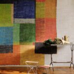 Kleurrijk Elitis-behang met abstracte blokpatronen in een interieur met metalen meubels en een bos bloemen op tafel.