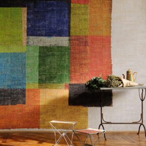 Kleurrijk Elitis-behang met abstracte blokpatronen in een interieur met metalen meubels en een bos bloemen op tafel.