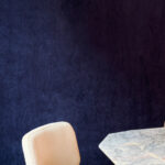 Luxe donkerblauw Elitis Alcove behang met een marmeren tafel en beige stoel.