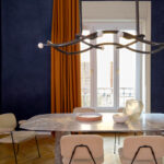 Luxe eetkamer met Elitis Alcove behang, marmeren tafel, moderne verlichting en oranje gordijnen.