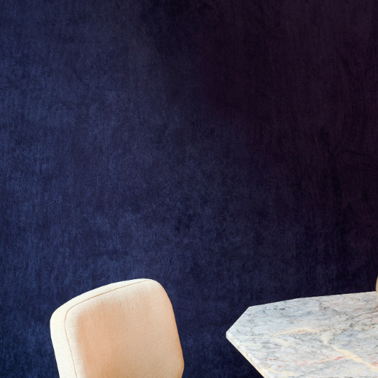 Luxe donkerblauw Elitis Alcove behang met een marmeren tafel en beige stoel.