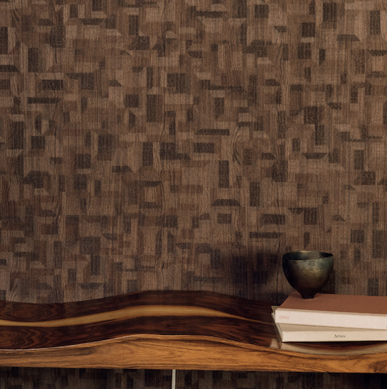 Donkerbruin Elitis-behang Bois Sculpté Ramille met geometrisch houtstructuurpatroon, gecombineerd met een golvende houten plank en decoratieve objecten.