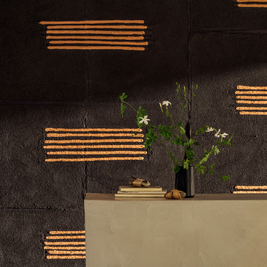 Zwarte muur met Elitis Hanji Noto RM 1058 80 behang en horizontale koperkleurige accenten, met een vaas bloemen en boeken op een beige console.