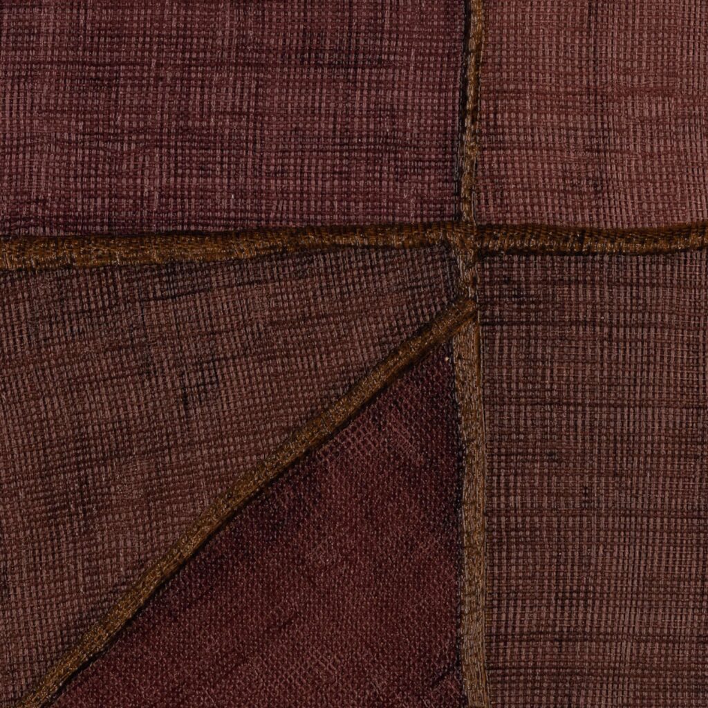 Detailopname van het Elitis-behang La Caravane Kungbo VP 944 09 met een patchworkstructuur in warme rood- en bruintinten.