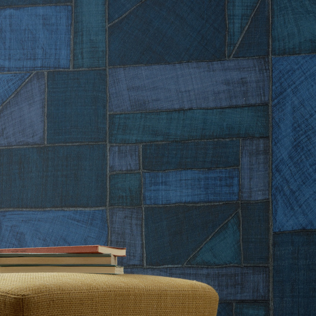 Geometrisch Elitis-behang La Caravane Kungbo VP 944 in verschillende blauwtinten met een poef en stapel boeken op de voorgrond.