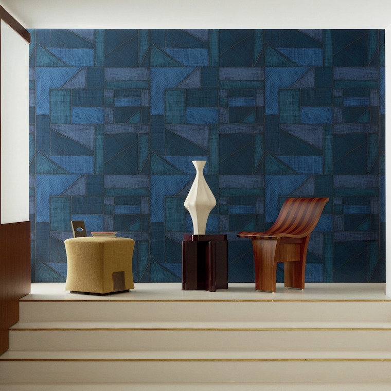 Moderne interieursetting met Elitis behang La Caravane Kungbo VP 944 in blauw, een designstoel, bijzettafeltjes en een decoratieve vaas.