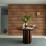 Ronde houten tafel met decoratieve vazen en boek, voor Elitis-behang La Caravane Moshi Moshi VP 942 05 in een moderne interieursetting.