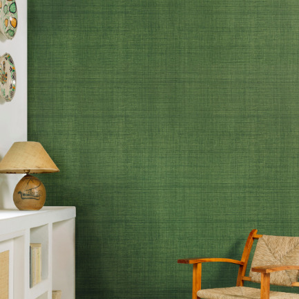 Woonkamer met Elitis behang in groentint uit de Matières Végétales Abaca collectie, naast een houten stoel en lamp op een wit kastje.