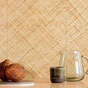Elitis behang uit de Matieres Végétales collectie met een natuurlijke geweven textuur, afgebeeld met kokosnoten, een glazen karaf en een keramisch kopje op een houten oppervlak.