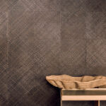 Donkerbruin Elitis-behang van plantaardig materiaal met geweven textuur, met een decoratieve mand op een houten tafel.