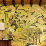 Sfeerbeeld van een interieur met het Elitis-behang 'Matières Végétales Costalegre VP 992 03', met een tropisch junglepatroon in gele en groene tinten.