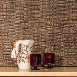 Witte decoratieve kan en twee rode glazen voor Elitis Raphia behang met natuurlijke textuur.