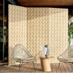 Twee rotan stoelen en een houten bijzettafeltje met vazen staan voor Elitis Merida Wall Entrelazados RM 1019 behang met een gevlochten patroon.