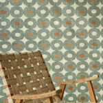 Groen Elitis Merida behang met retro geometrisch patroon en houten stoel met geweven zitting.