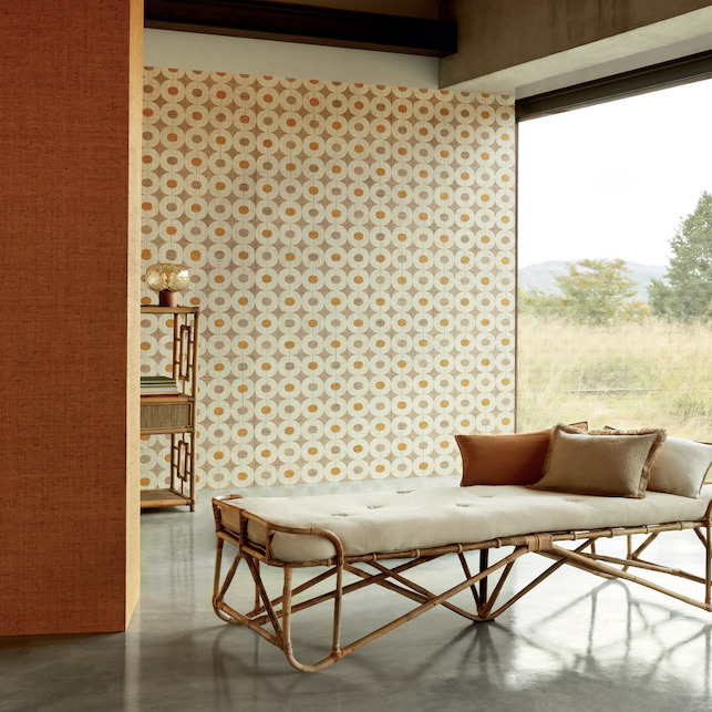Luxe interieur met Elitis Merida behang (model Pepite RM 1018) in warme aardetinten en rotan ligbank bij een grote raampartij.