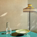 Moderne interieursetting met Elitis Merida behang, een glazen karaf, een decoratief bord en een design vloerlamp.