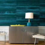 Modern interieur met Elitis-behang Mouvements Esprit Libre in blauwgroene tinten, metalen kast, designlamp en decoratieve krukjes.