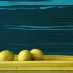 Drie citroenen op een gele schaal voor een donkerblauw Elitis-behang met abstract patroon uit de Mouvements Esprit Libre collectie.
