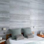Sfeervolle slaapkamer met Elitis-behang Mouvements Esprit Libre RM 1024 92 in grijstinten achter een bed met sierkussens.