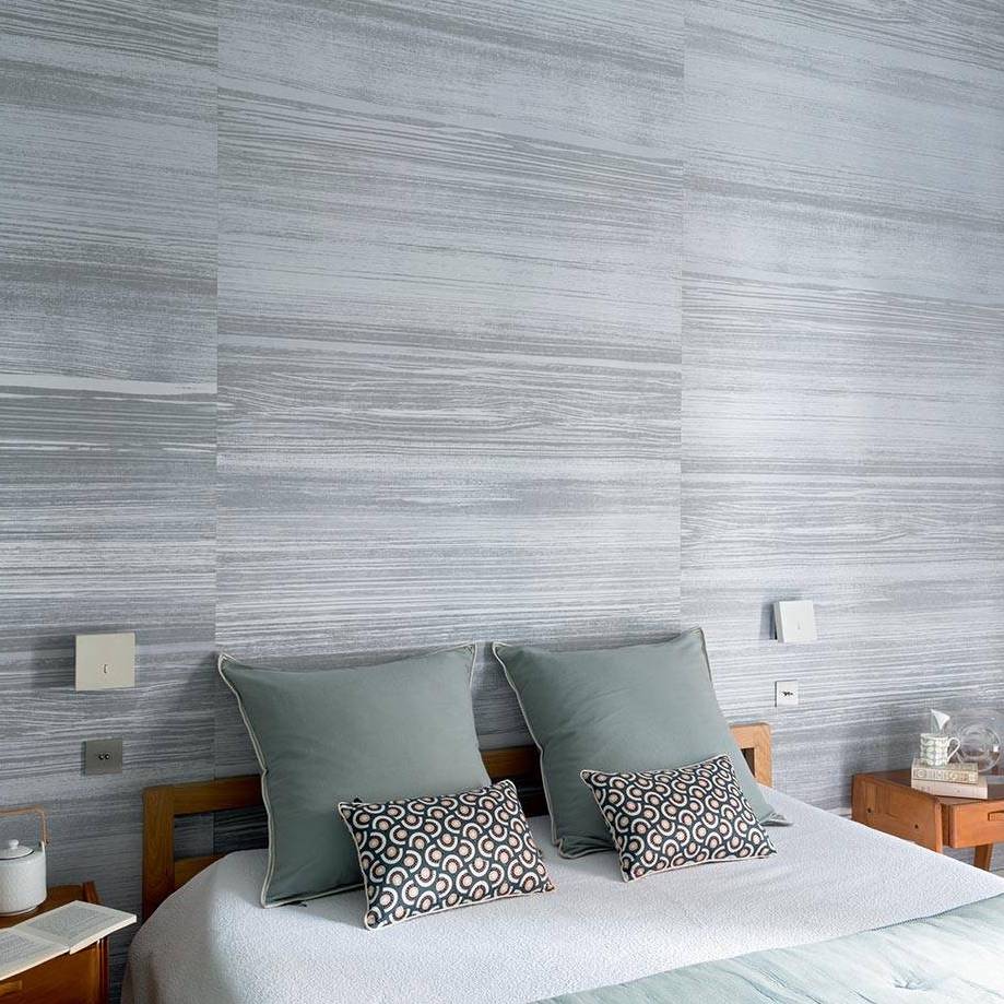 Sfeervolle slaapkamer met Elitis-behang Mouvements Esprit Libre RM 1024 92 in grijstinten achter een bed met sierkussens.