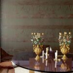 Luxe interieur met Elitis-behang Mouvements Impulsion RM 1022 65, gouden kandelaars en een ronde glazen tafel.