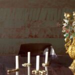 Close-up van een interieur met Elitis-behang Mouvements Impulsion RM 1022-65, een glazen tafel met moderne kandelaars en een decoratieve gouden kandelaar.