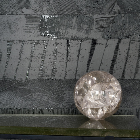 Glanzend Elitis-behang uit de Mouvements Impulsion RM 1022 90 collectie met abstract patroon, gecombineerd met een decoratieve glazen bol op een glazen oppervlak.