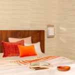 Sfeervolle slaapkamer met Elitis Betty PL 308 35 02 Amarante wandbekleding, warme kussens en opengeslagen boek op bed.