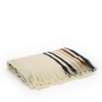 Opgevouwen Elitis Betty PL 308 86 02 Nuit plaid van crèmekleurige stof met franjes en gekleurde strepen.
