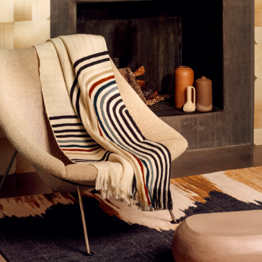 Designstoel met een Elitis Betty PL 308 86 02 Nuit plaid gedrapeerd in een warme, moderne interieursetting.