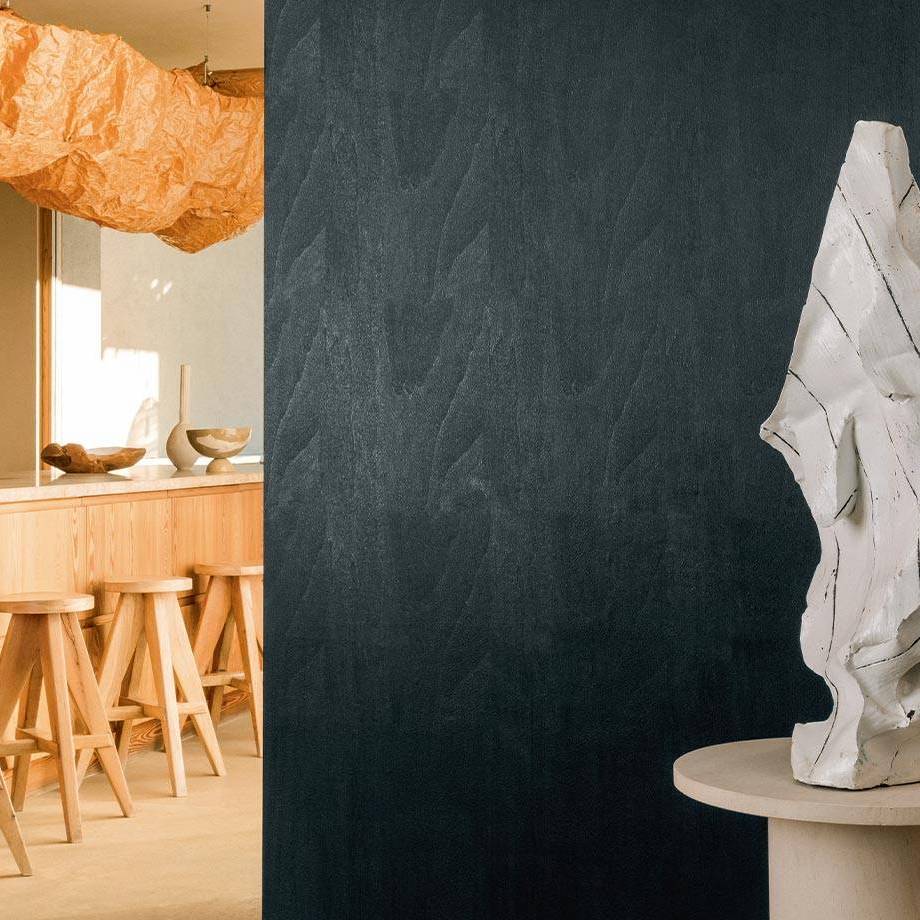 Moderne interieursetting met een donker Elitis Bois Sculpte Gouge wandpaneel, houten barkrukken en een abstract wit beeld.