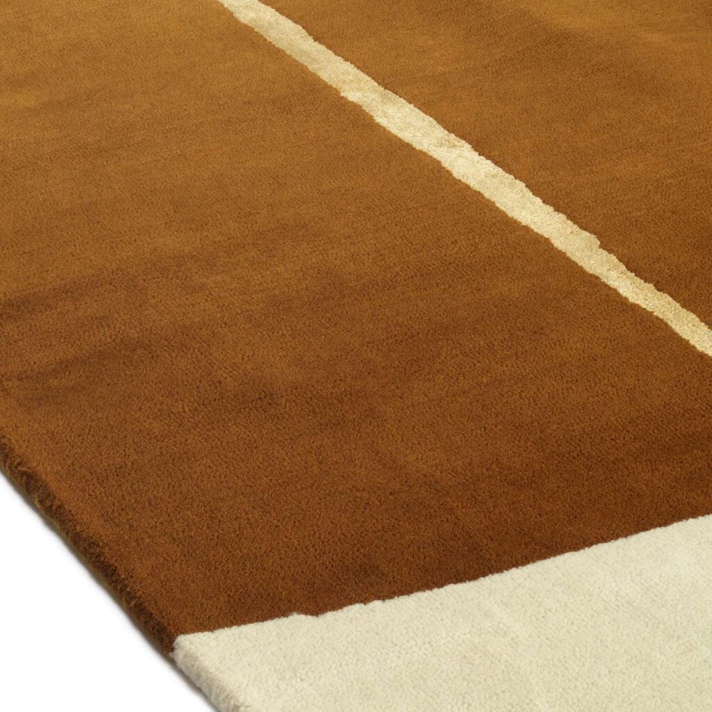 Detail van het Elitis Celeste TA 133 25 02 vloerkleed met een warme bruine kleur, een lichte middenstreep en een wit hoekvlak.